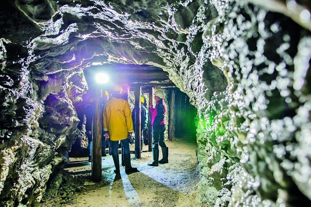 Geführte Besuchergruppe mit Schutzhelmen im beleuchteten Stollen des Schaubergwerks Arzberg.