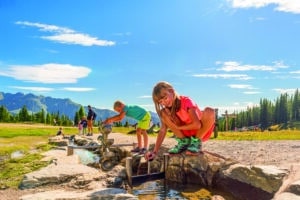 Kinder spielen an einer Wasserstation im Hopsiland Planai vor steirischer Bergkulisse.