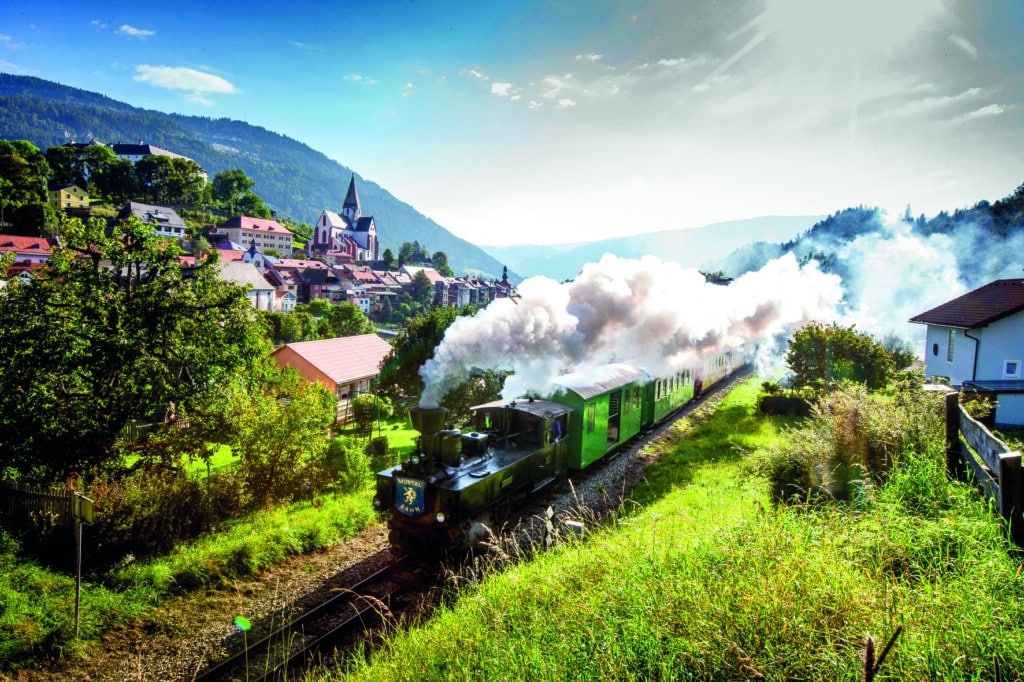 Dampfzug der Murtalbahn fährt mit grünen Waggons durch Murau im Oberen Murtal.