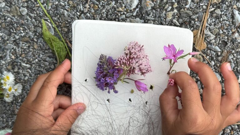 Kind steckt Wildblumen durch die Löcher der Naturvase aus Karton