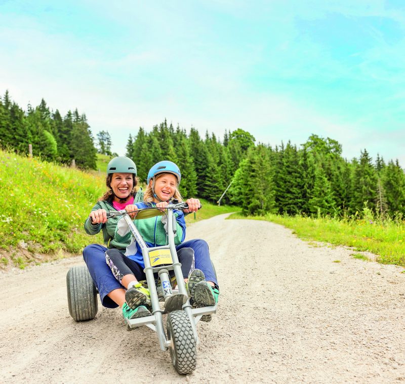 Erwachsene und Kind fahren mit einem Mountaincart auf der Gemeindealpe Mitterbach ins Tal.